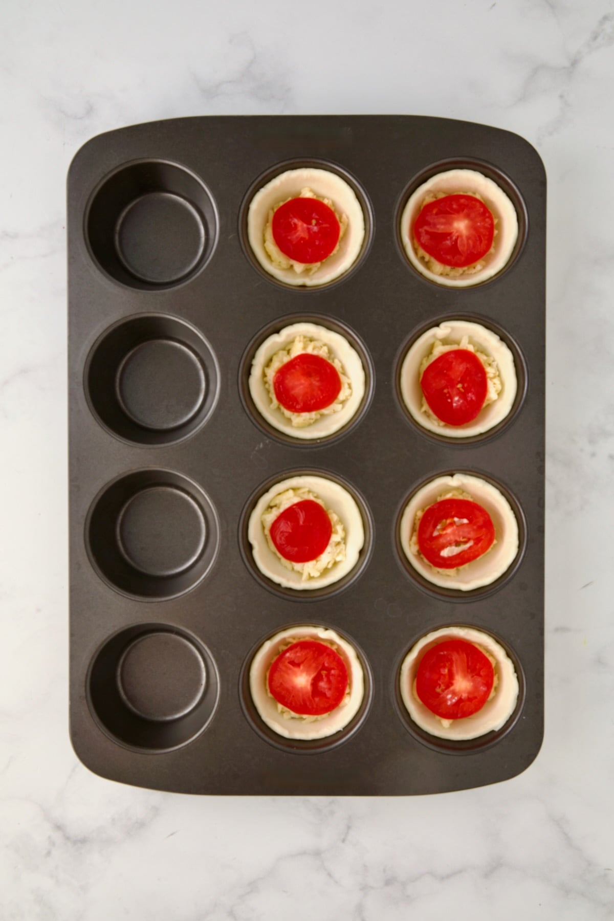 Slices of tomato placed over mayonnaise and cheese mixture in a 12-cup metal muffin pan.