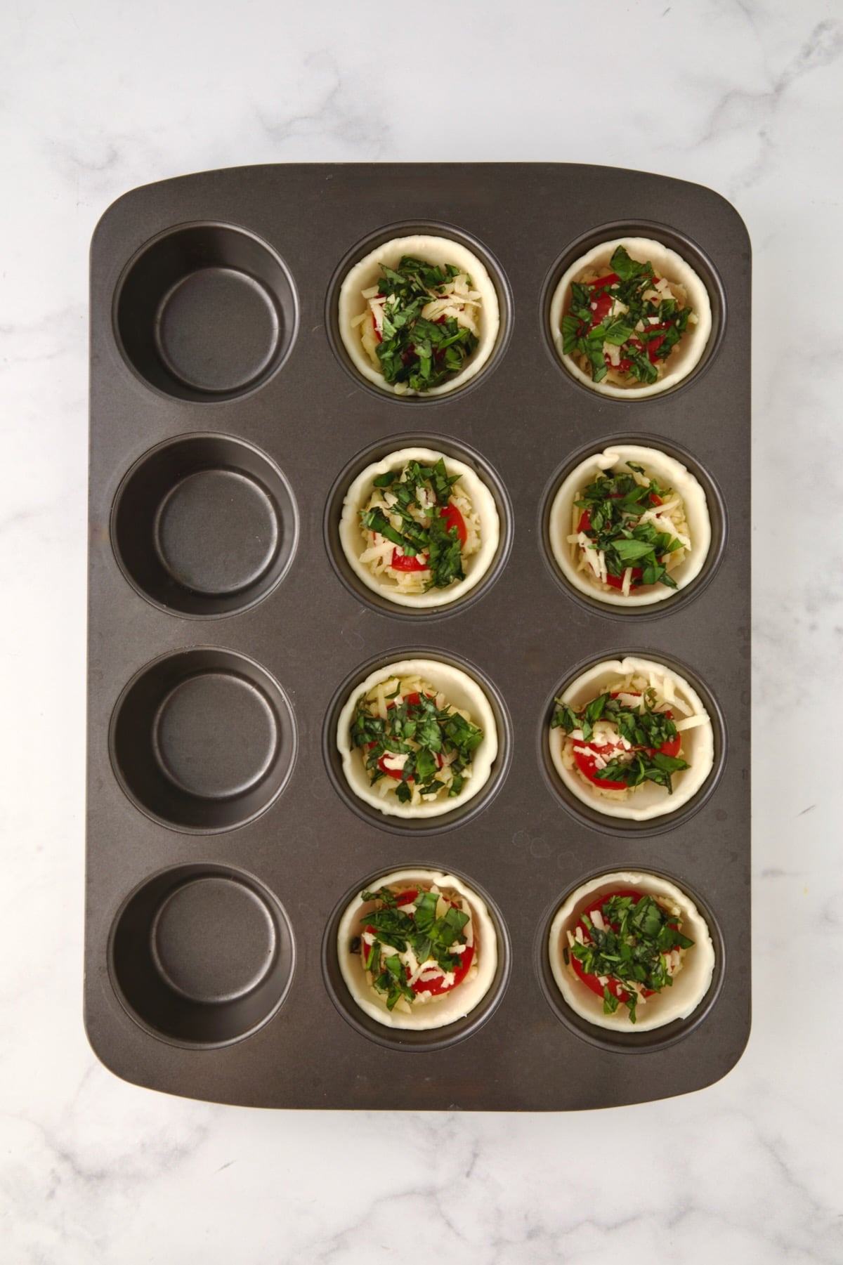 Fresh chopped basil added over grated cheese in a 12-cup muffin pan.