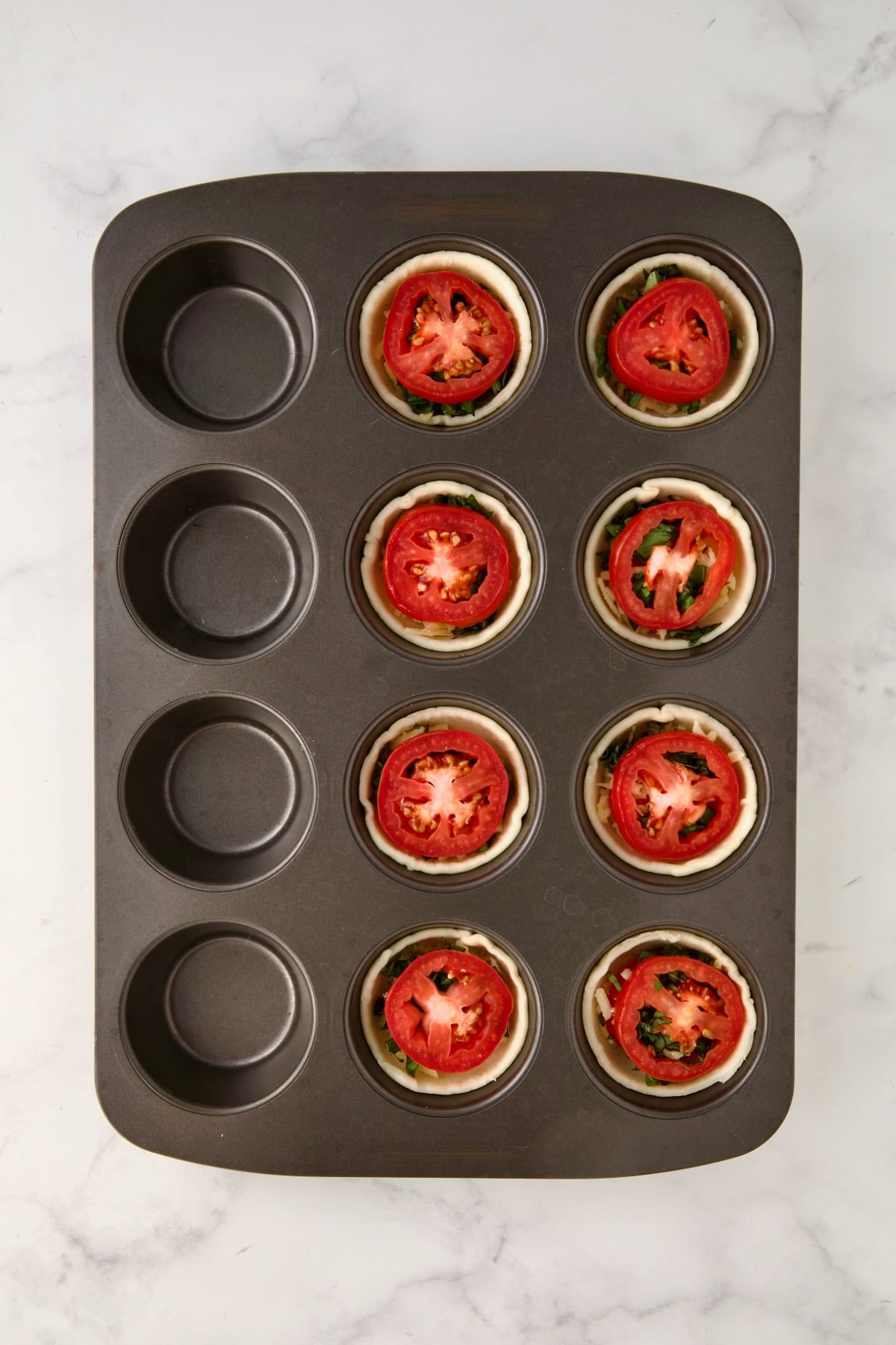 Layer of tomatoes placed over basil in a 12-cup metal muffin pan.