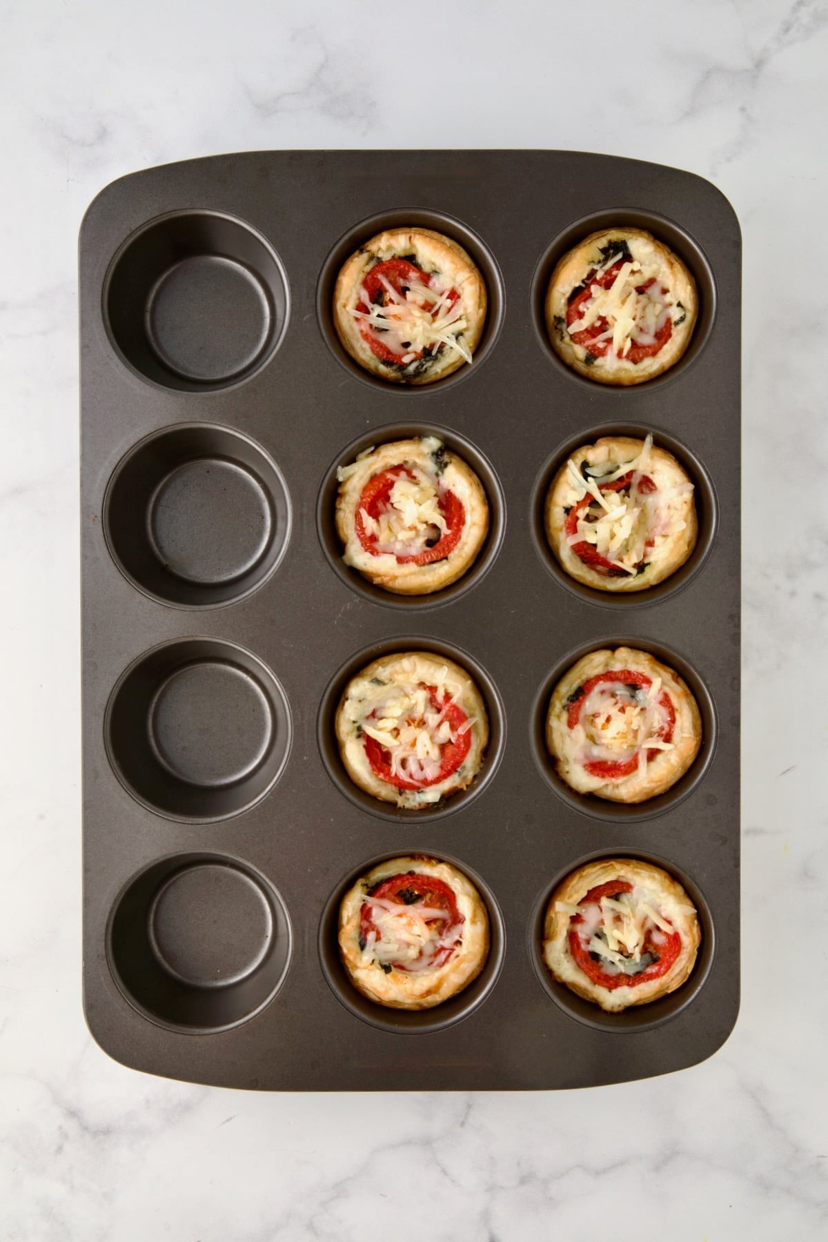 Partially baked Mini Southern Tomato Pies in 12-cup metal muffin pan.
