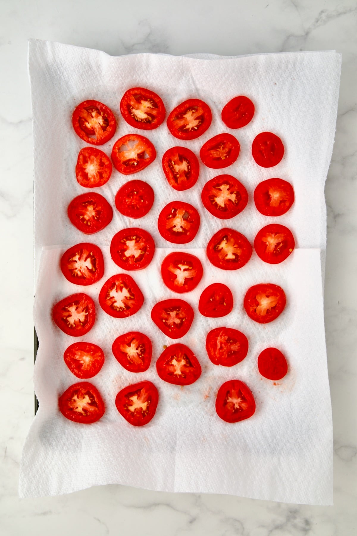 Sliced plum tomatoes on paper towel lined rimmed baking sheet.