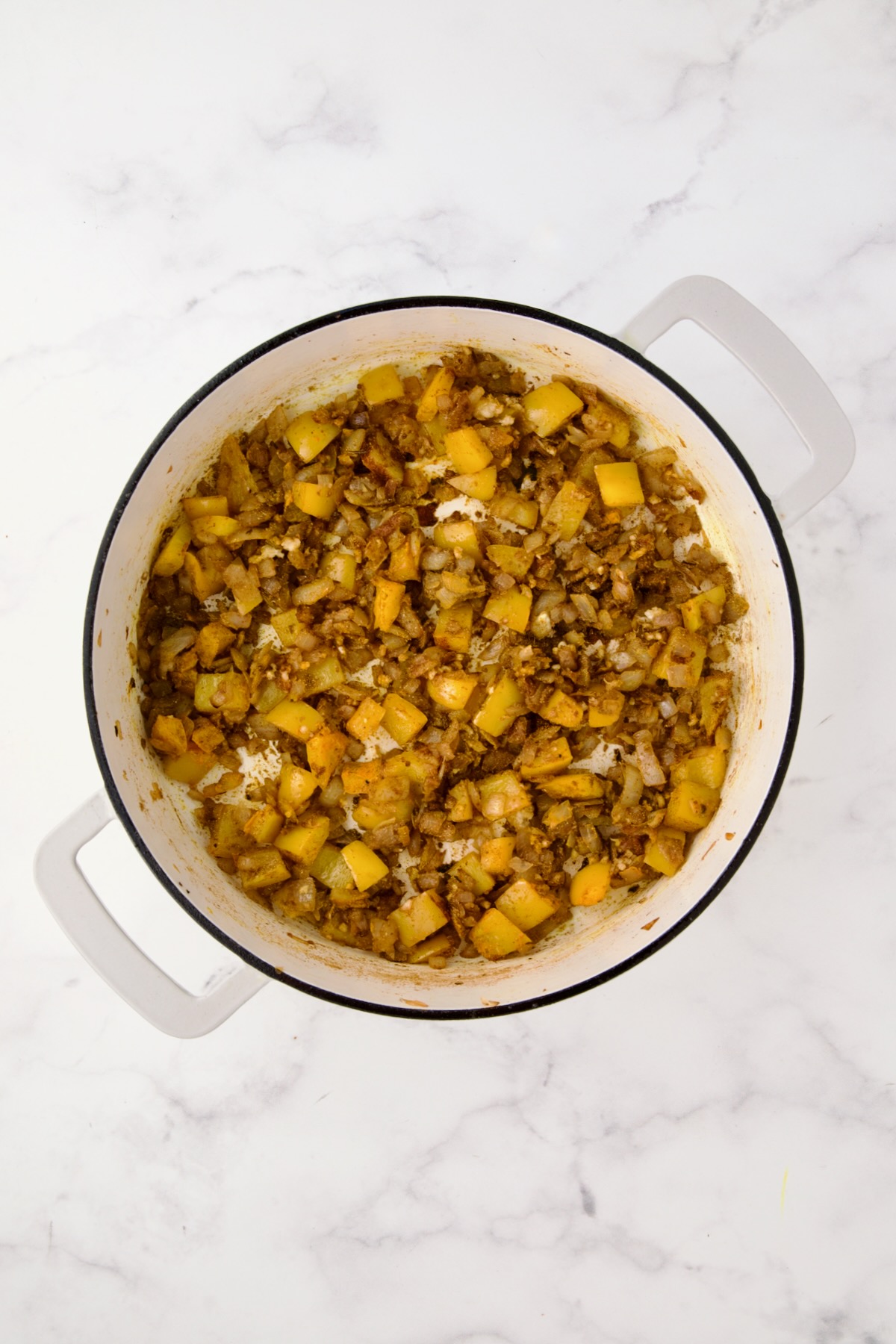 Sauteed spices mixed into onions and yellow bell pepper in white enamel cast iron skillet.