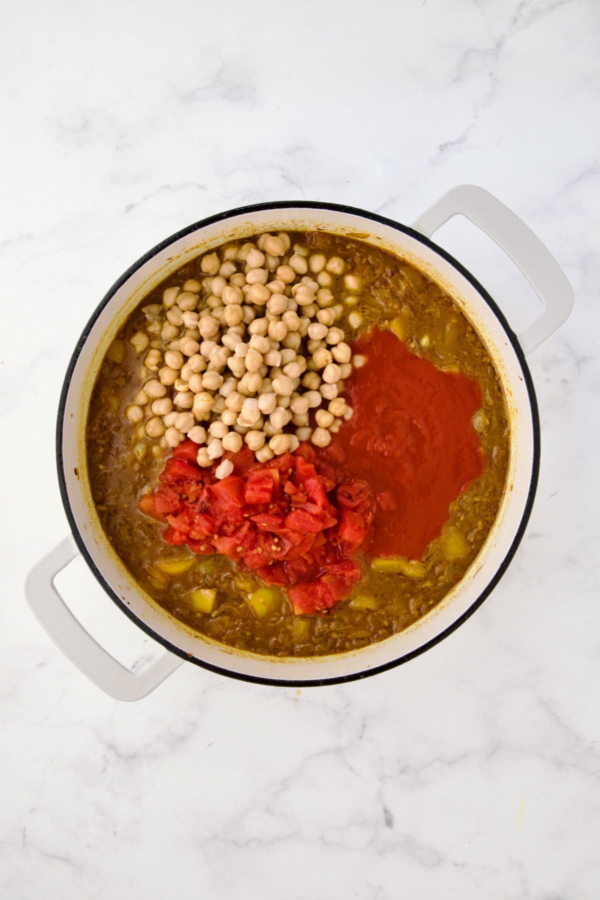Chickpeas, diced tomatoes and tomato sauce added to onions, yellow bell pepper and spices in white enamel cast iron skillet.