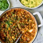 Finished Moroccan Eggplant Stew in white enamel cast iron skillet with bowl of couscous.