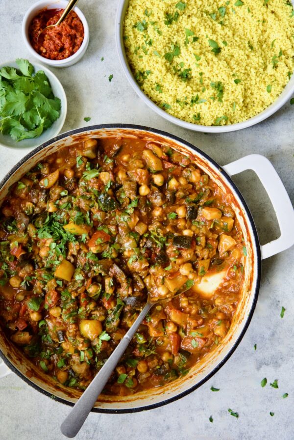 Finished Moroccan Eggplant Stew in white enamel cast iron skillet with bowl of couscous.