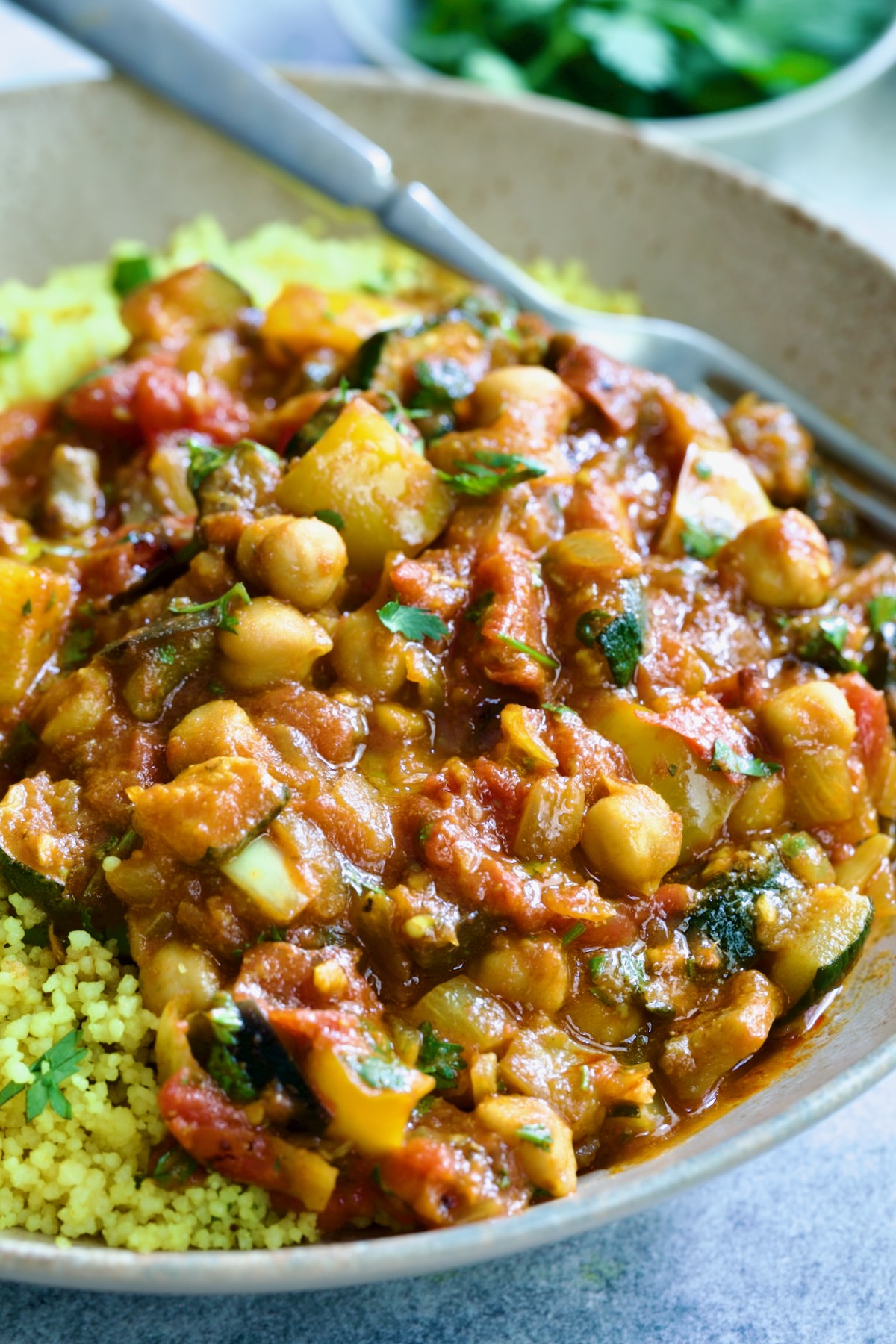 One serving of Moroccan Eggplant Stew and couscous in earthenware bowl with dinner fork.