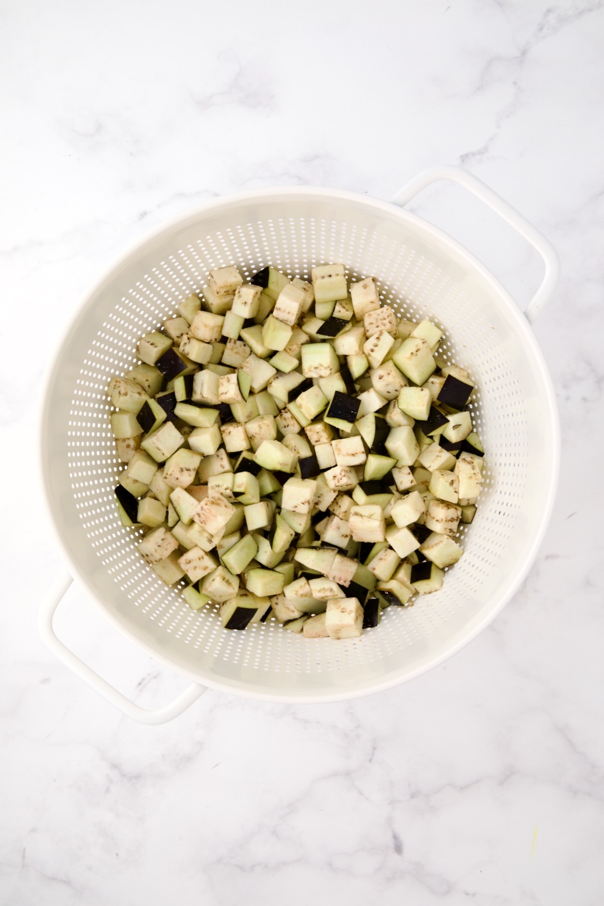 Cubed eggplant in white colander before being drained.