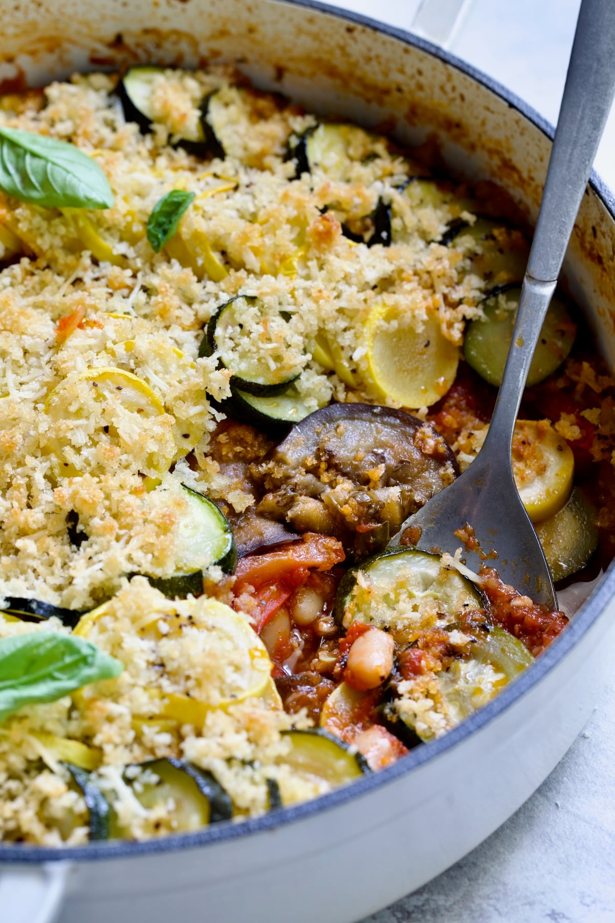 Summer Vegetable Cassoulet in white enamel cast iron skillet with serving spoon scooping some up.